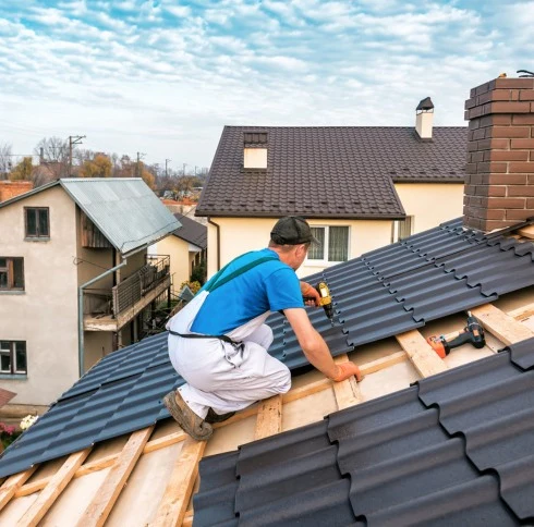 This image shows a professional roofer wearing a blue shirt, white overalls, and a cap, working on a sloped roof.